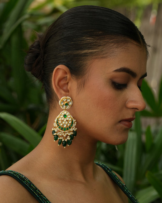 Woman wearing gold and green earrings with a blurred green background