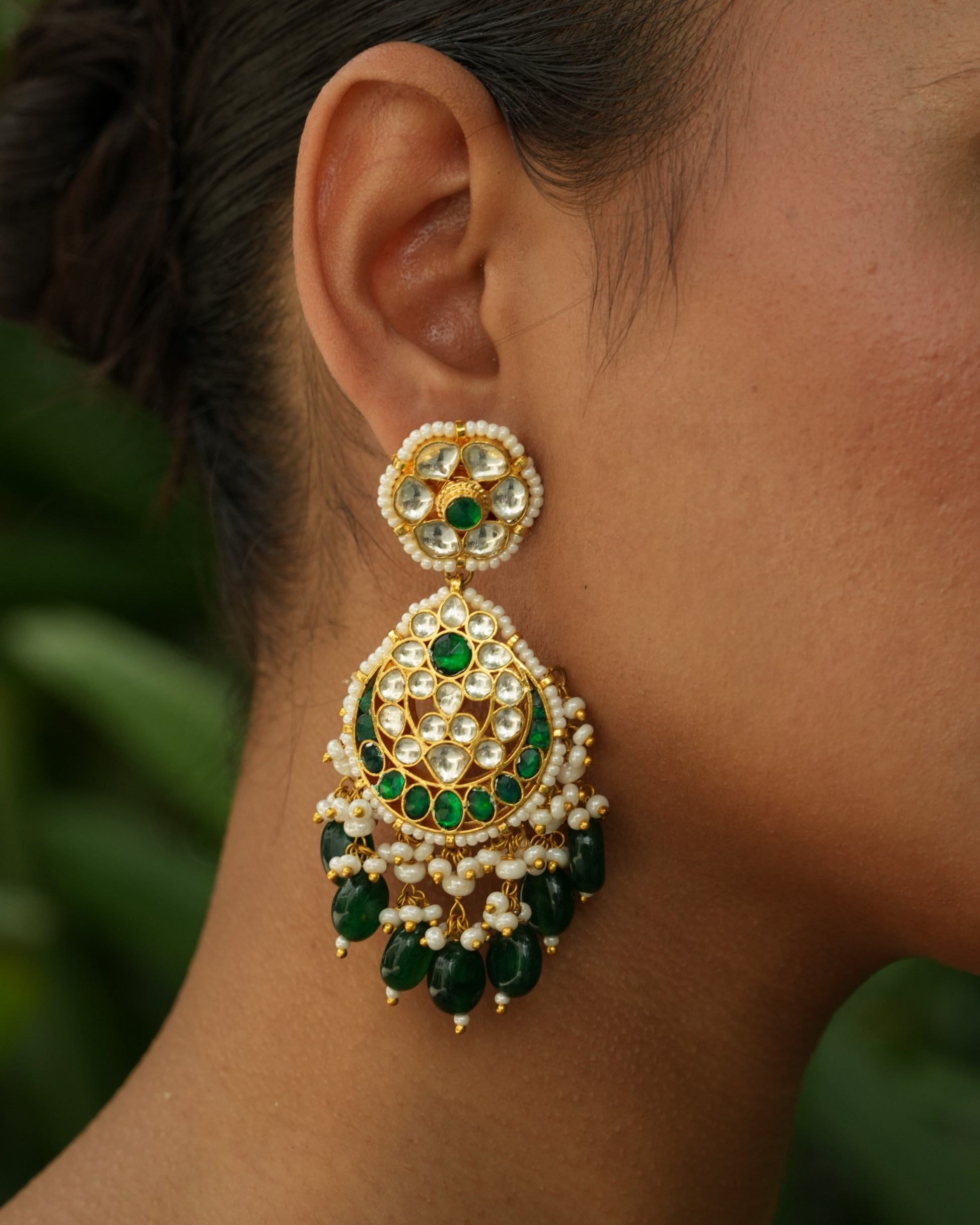 Close-up of an ear wearing a decorative earring with green gemstones and gold accents.